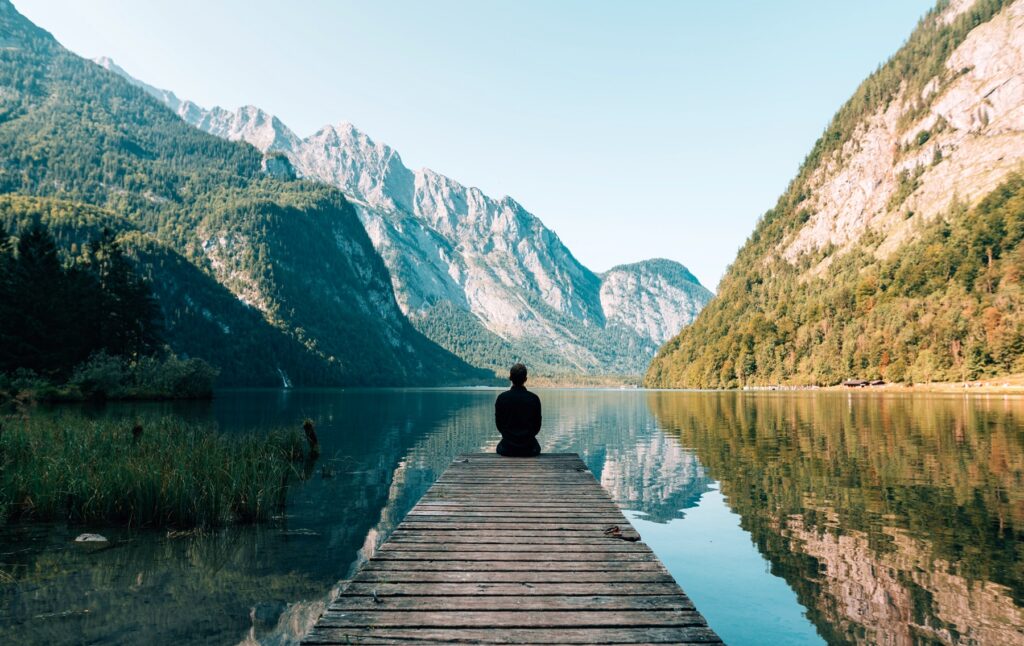 Symbolbild Jin Shin Jyutsu Frieden: Mensch sitzt auf Steg über ruhigem See