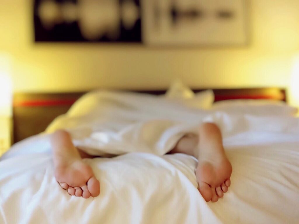 Symbolbild für Jin Shin Jyutsu bei Müdigkeit: Mensch liegt zugedeckt im Bett, nur die Füße ragen hervor